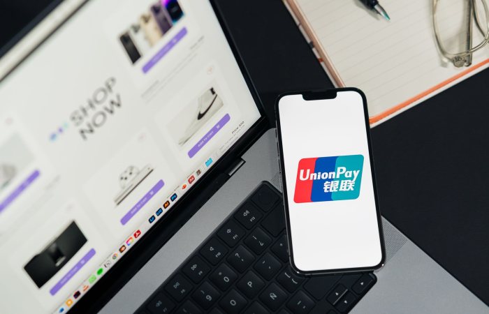 UnionPay logo displayed on a smartphone next to a laptop with an online shopping page open.