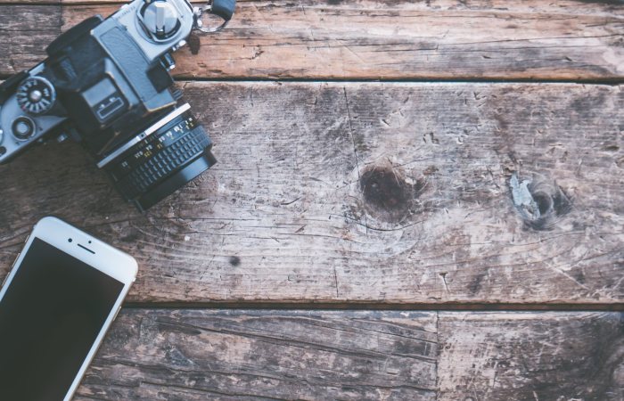 A vintage camera and smartphone on a rustic wooden surface, highlighting technology contrast.