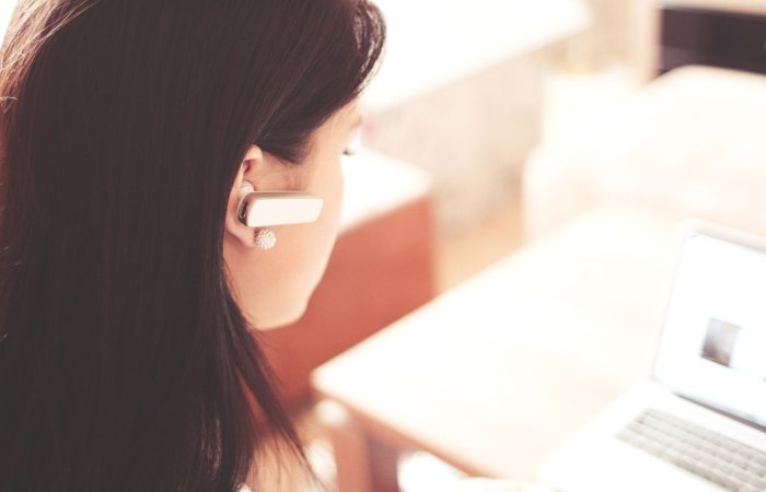 A businesswoman using a Bluetooth headset while working on her laptop in a modern office.