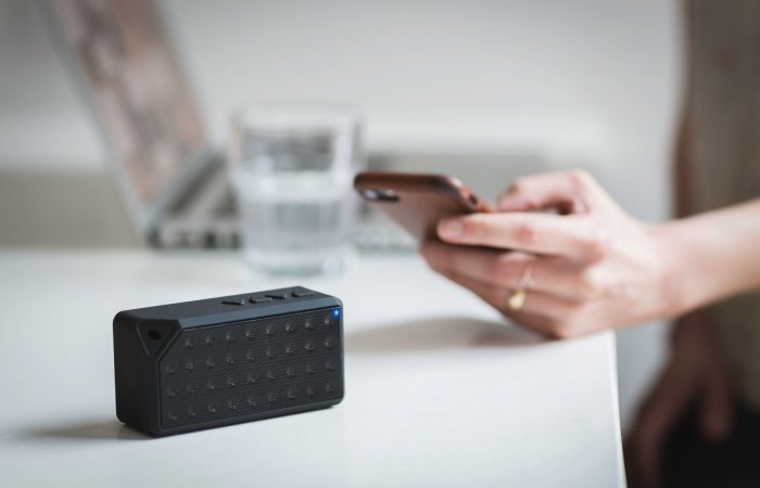 Person connecting a smartphone to a wireless speaker indoors, foreground focus.