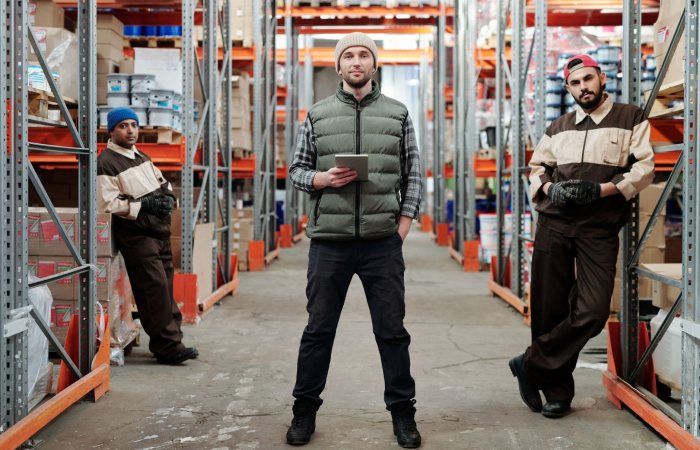 Three men in a warehouse standing among shelves with inventory.