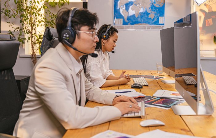Call center agents working at computers with headsets in a modern office setting.