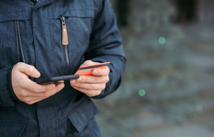 Crop anonymous male in casual clothes entering credit card details on smartphone on street in daylight