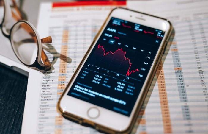 Close-up of smartphone with stock market graph on table with financial documents and glasses.