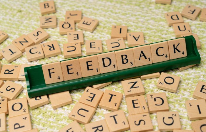 Wooden letter tiles spelling 'feedback' on a green rack, representing communication and evaluation.