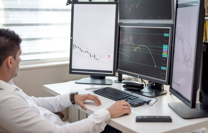 A businessman at his desk analyzing financial charts on multiple monitors.