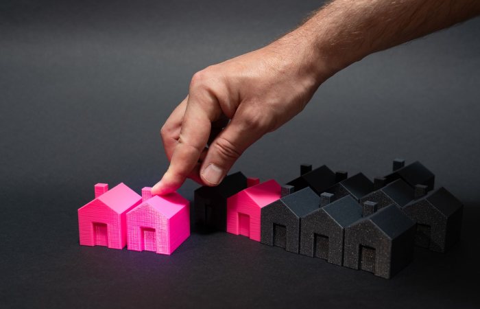 A hand choosing a vibrant pink house model among black miniatures, symbolizing real estate selection.